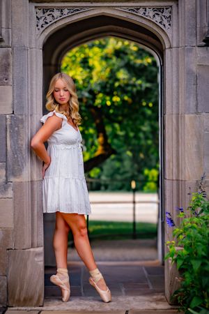 Senior ballerina posing on pointe outdoors with soft natural light and warm colors.