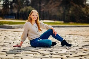 High school senior posing confidently outdoors with a natural smile, dressed in stylish attire, with soft golden sunlight