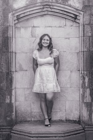 High school senior posing confidently outdoors with a natural smile, dressed in stylish attire, with soft black and white filter