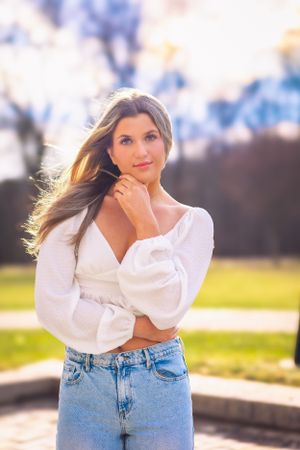 High school senior posing confidently outdoors with a natural smile, dressed in stylish attire, with soft golden sunlight highlighting their