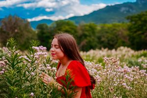 Stunning background of picturesque mountains and a clear blue sky with a young woman smelling flowers in the foreground