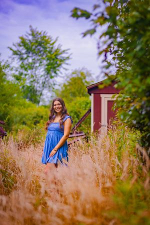 Standing out in a field of grass, young woman in blue dress strikes a pose
