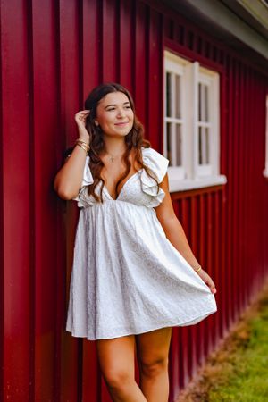 Young woman tucks a strand of hair while leaning against bright red barn