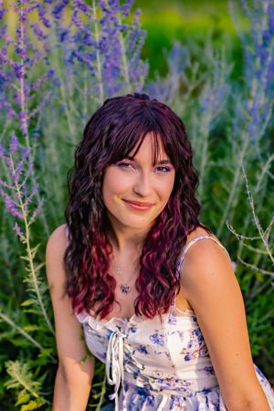 Woman with long red hair wearing floral dress in field of purple flowers.