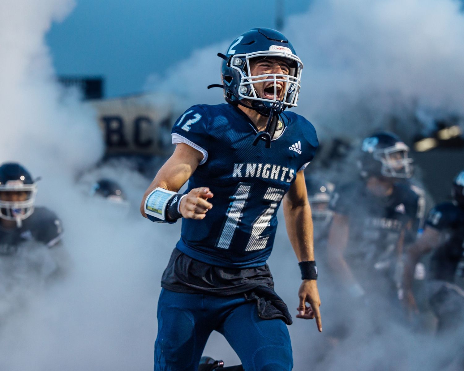 High School Football player yells intensely as he runs through tunnel and fog with teammates during pre-game ceremony.