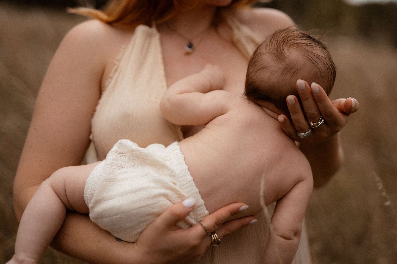 A mother breastfeeding her newborn baby wearing a white diaper in a tender moment outdoors.