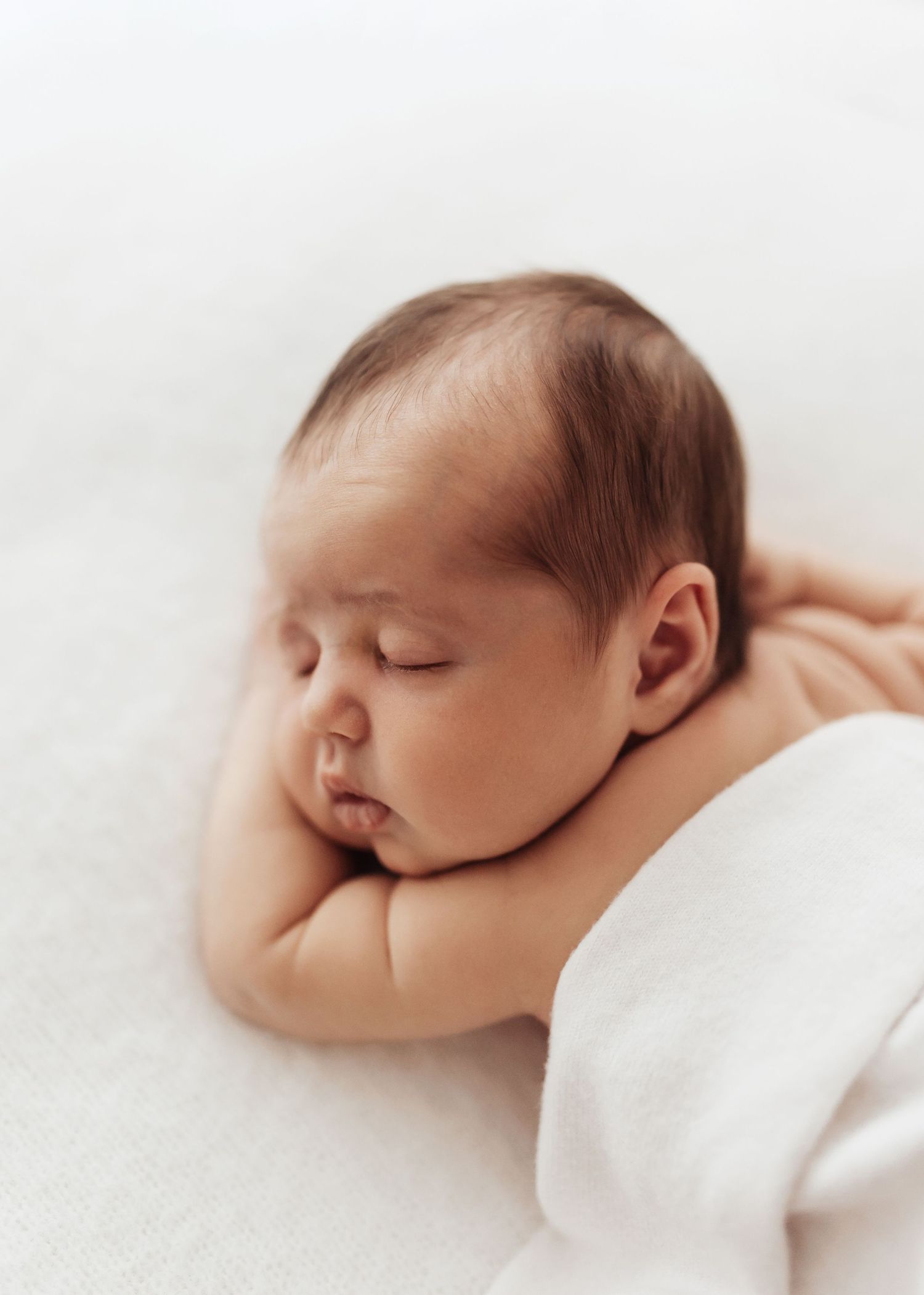 Peaceful newborn baby sleeping soundly wrapped in cozy white knit blanket.