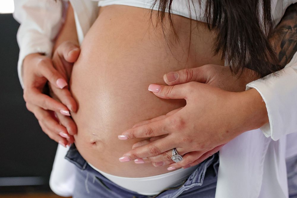Close up view of hands cradling a pregnant belly against dark background.