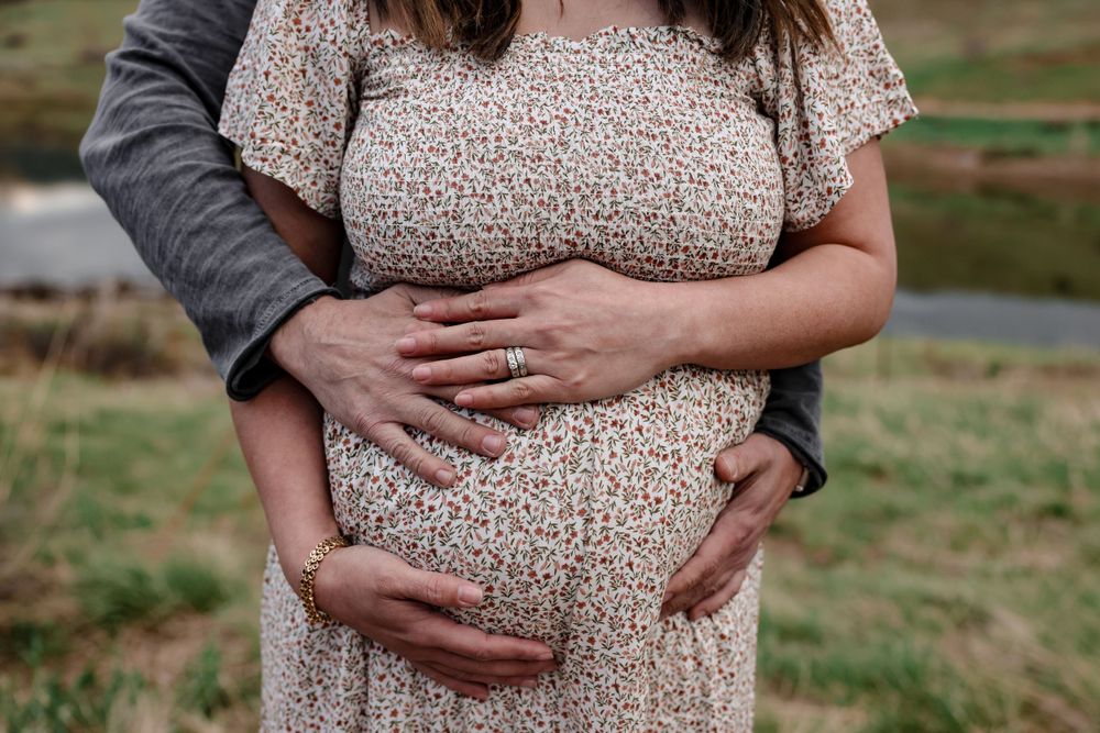 Close up of hands embracing pregnant belly in floral dress outdoors.