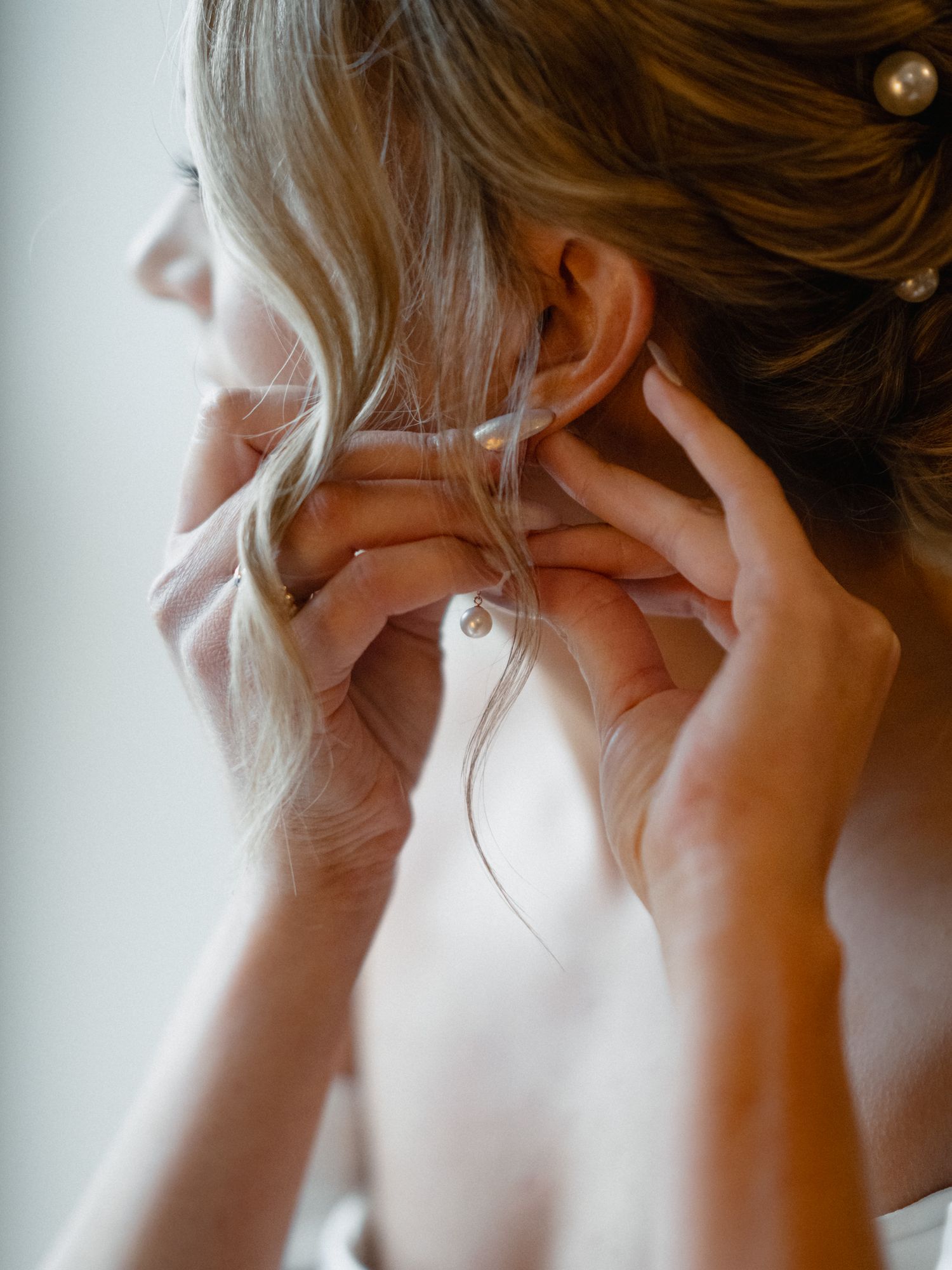 Side profile of bride adjusting earrings during wedding preparations.