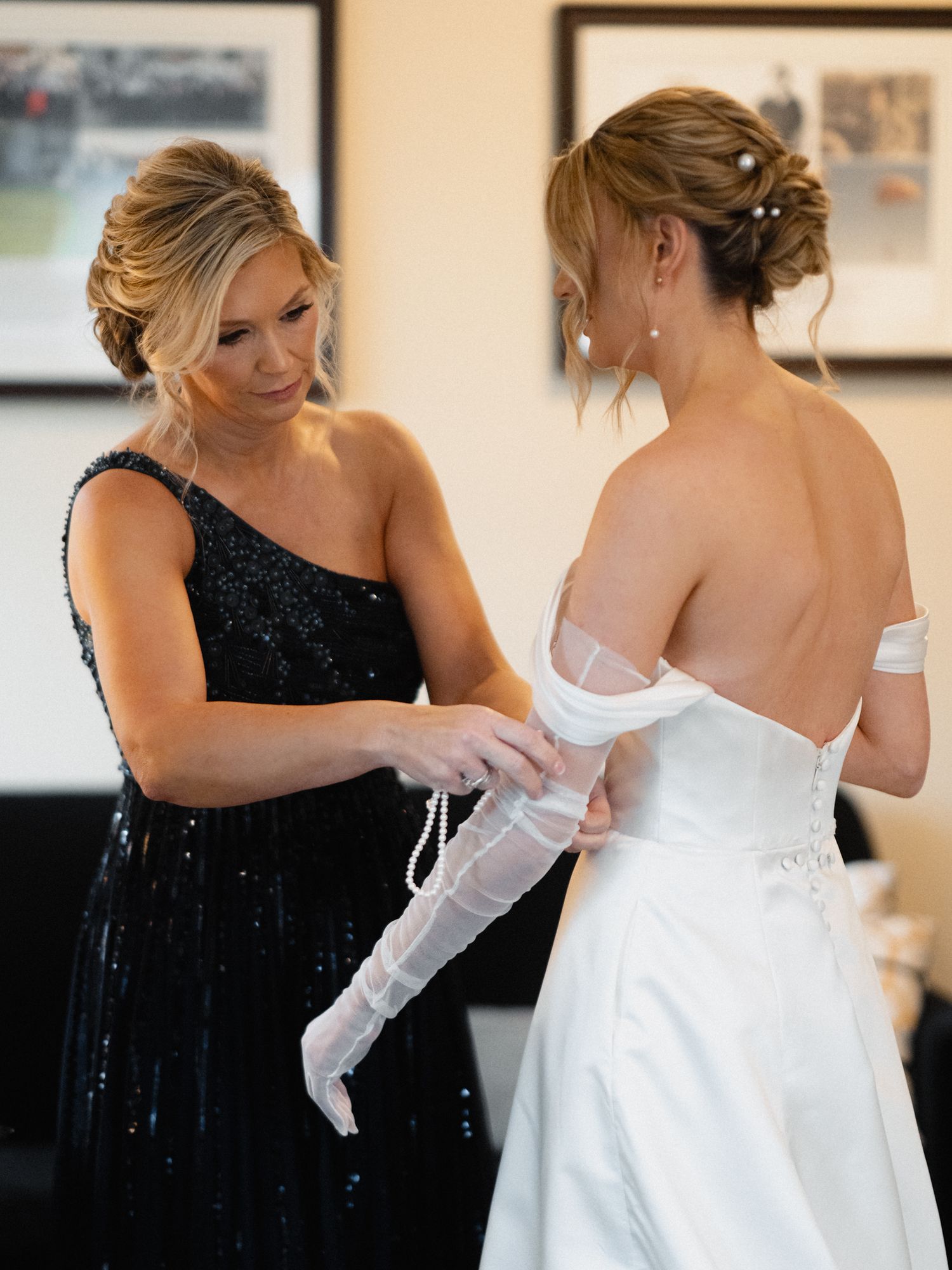 Helper in black dress assisting bride with white wedding gown sleeves.