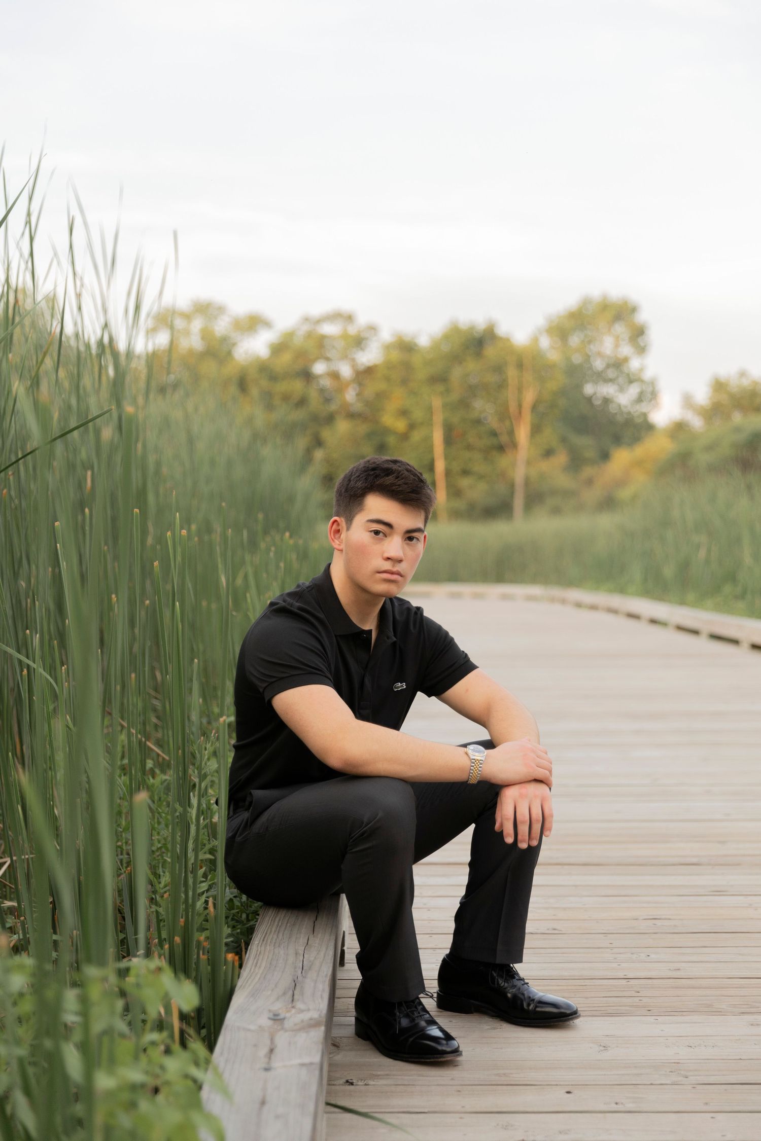teenage boy sitting on a wooden boardwalk in Rochester Hills at innovation hills park
