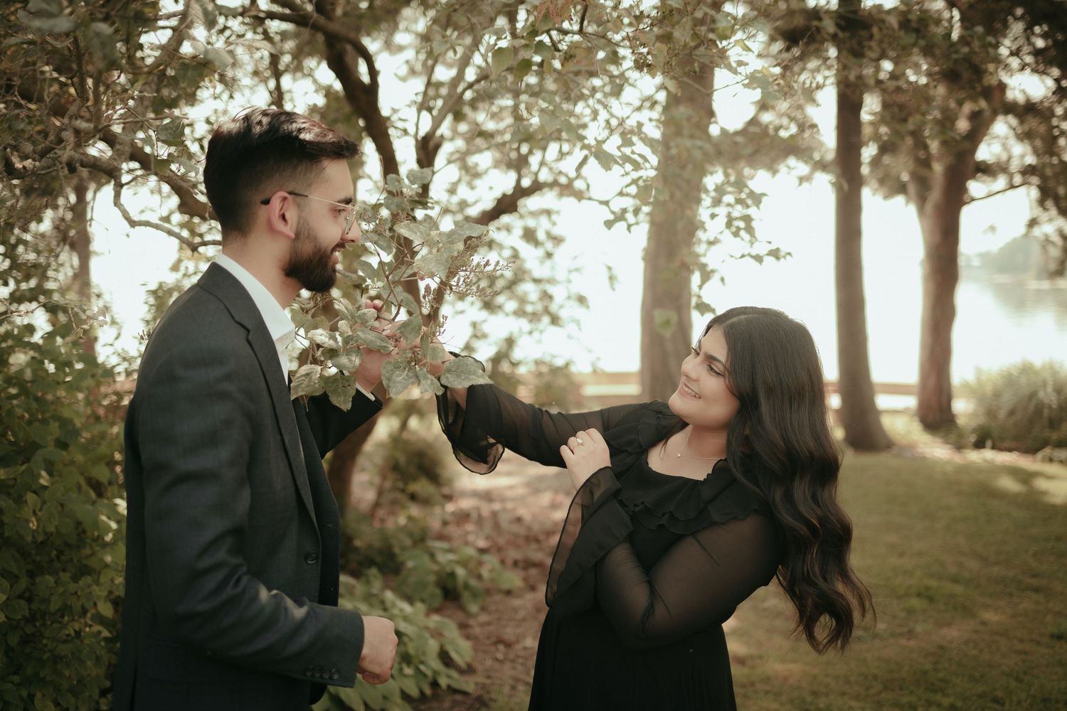 Playful moment between couple in formal attire against sunset-lit trees.