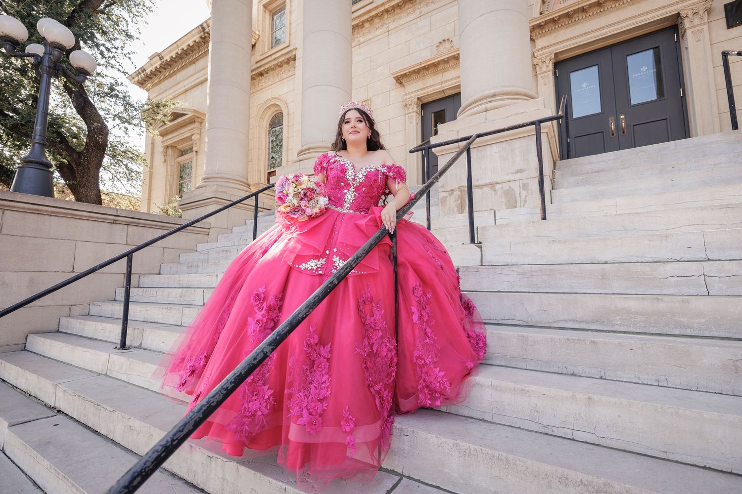 A vibrant pink ball gown displayed on historic stone steps of a classical building.