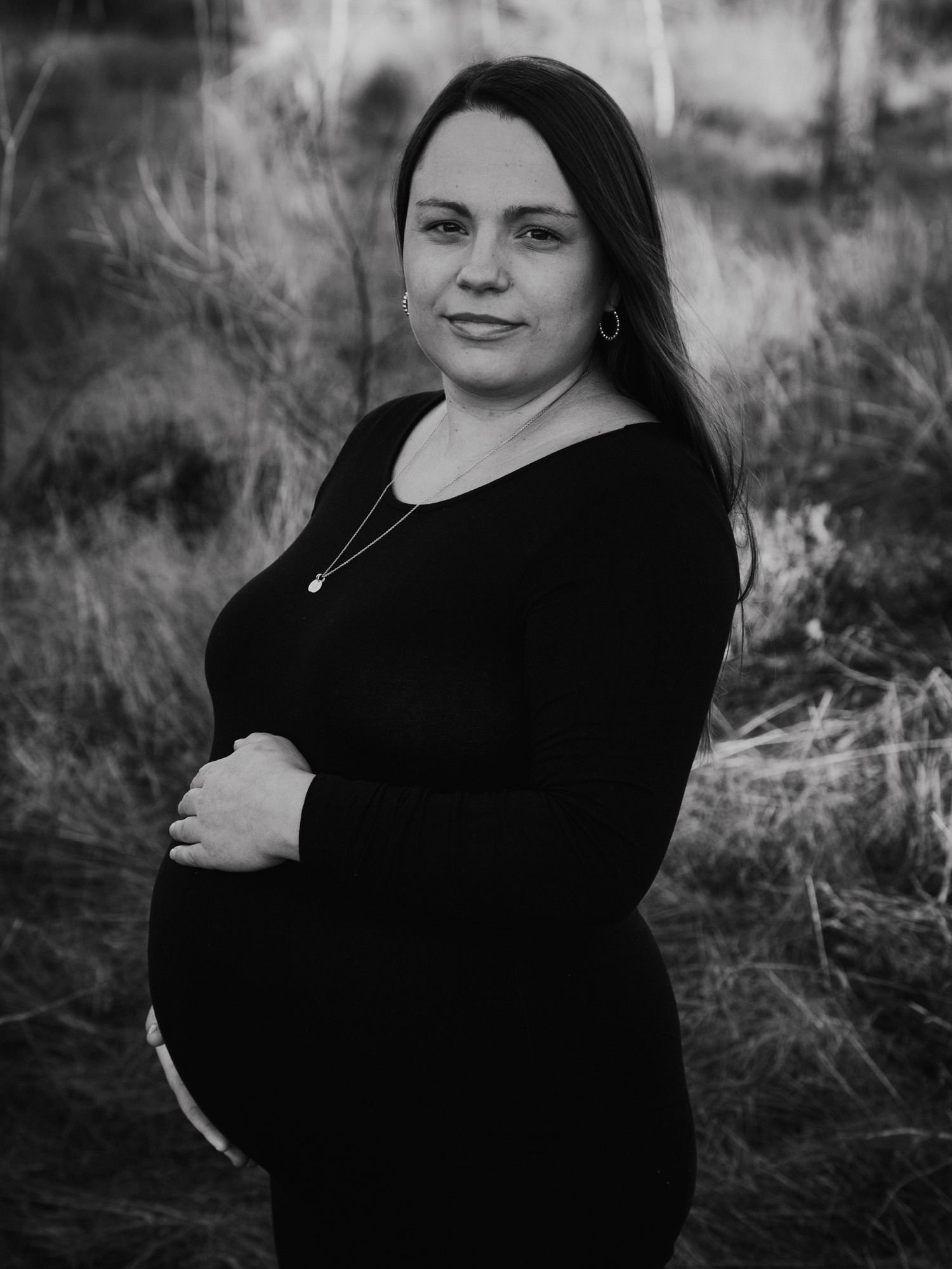 Gravid kvinna i svart klänning står i gräsfält