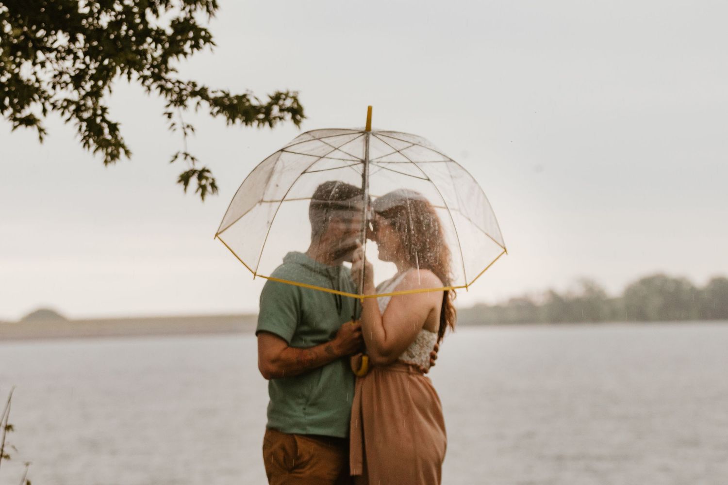 Romantic couple sharing an intimate moment under a clear umbrella by a serene lake.