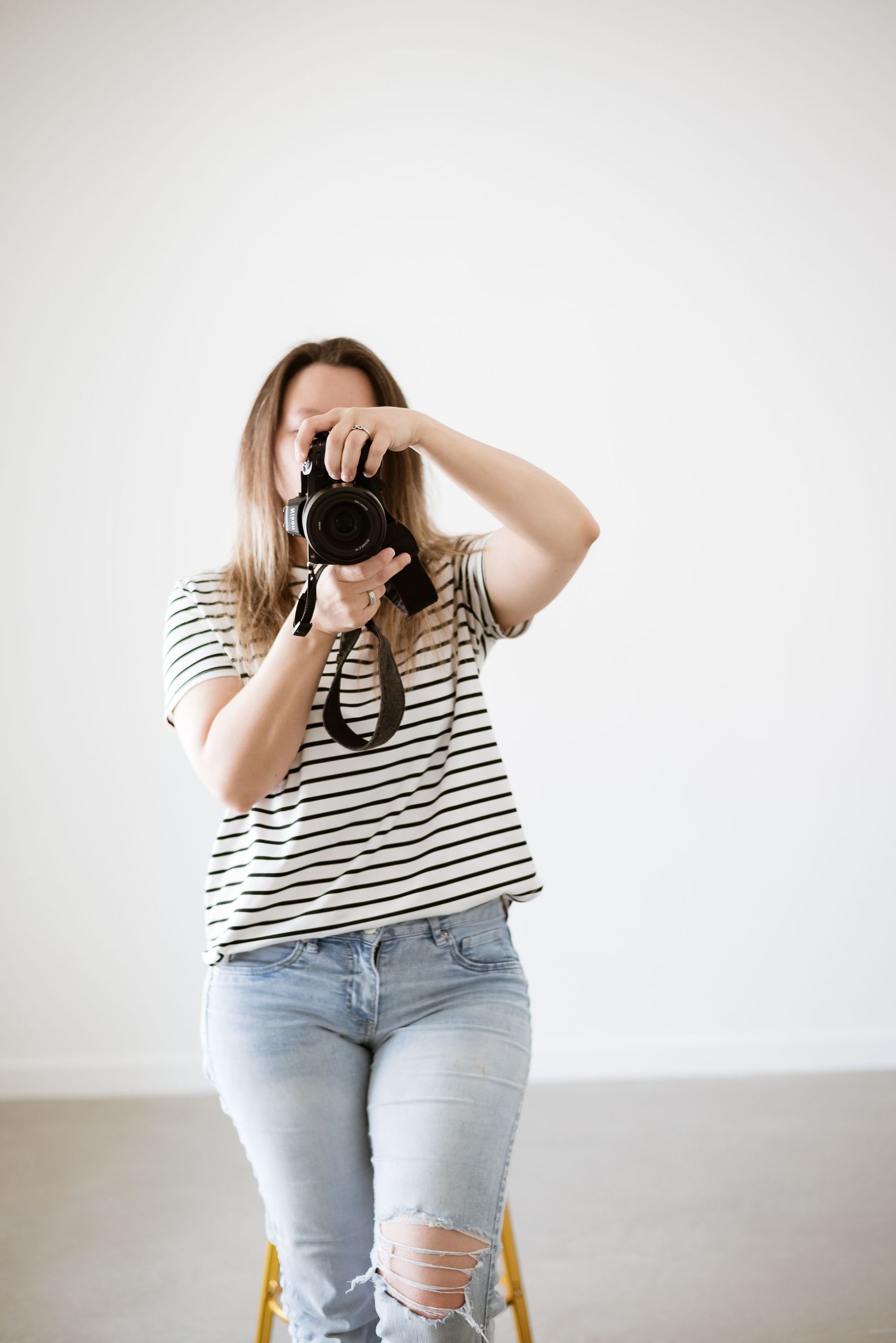 Photographer in striped shirt and ripped jeans taking pictures with professional camera.