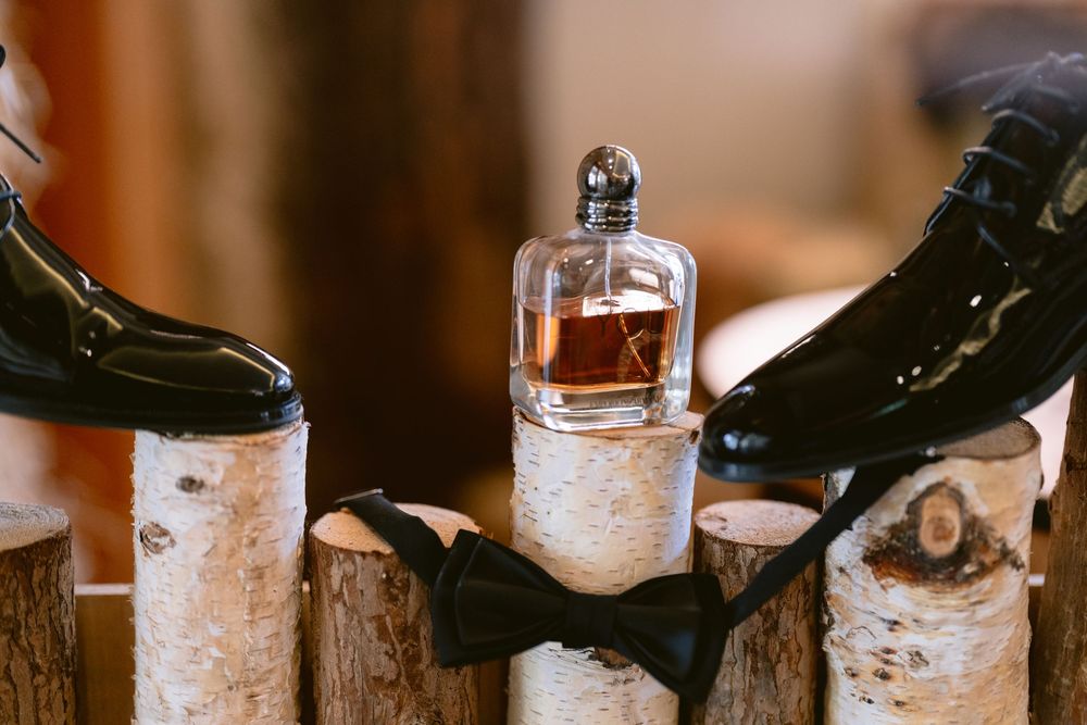 Groom accessories flat lay with black patent leather shoes, cologne bottle, and bow tie on birch logs.