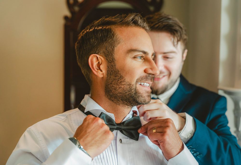 Wedding preparation moment as groomsman helps adjust bowtie before ceremony.