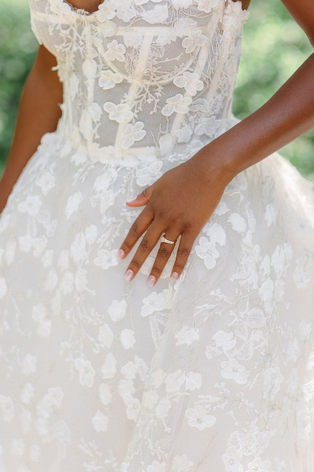 Close-up of a delicate white lace wedding dress and an engagement ring on a hand.