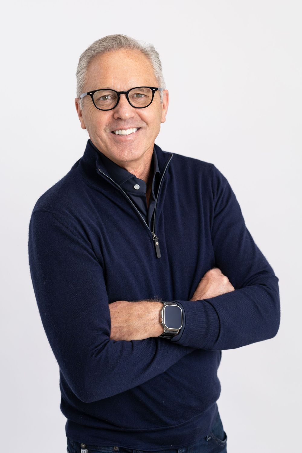Person wearing a navy blue sweater and glasses smiles confidently against white background in professional headshots.