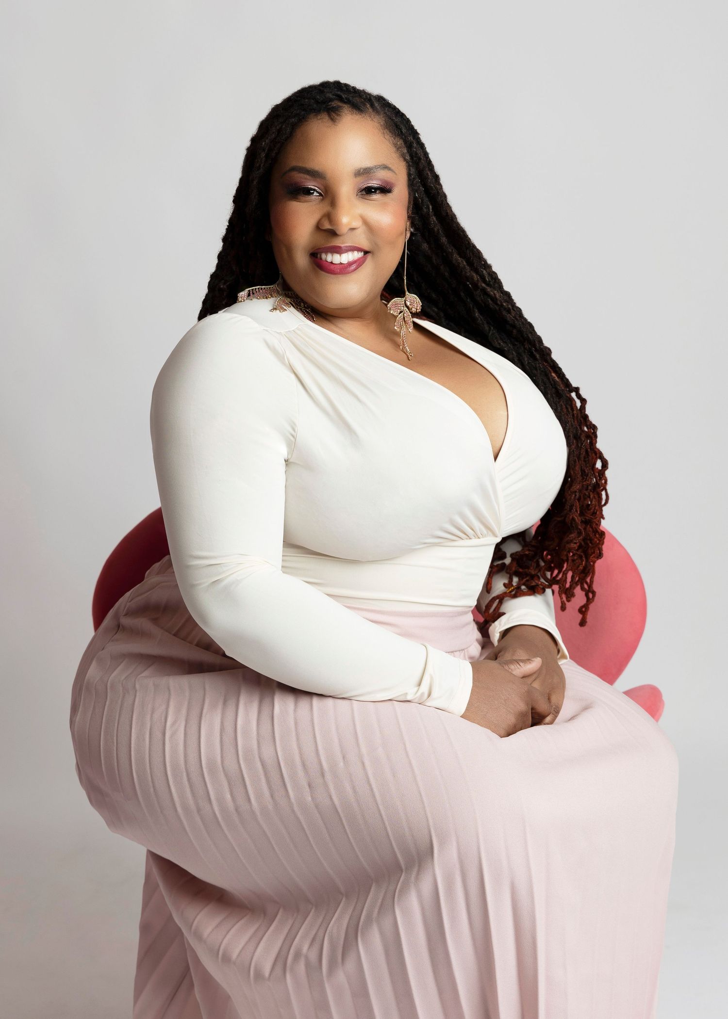 Portrait of a woman in white top seated elegantly on pink chair.