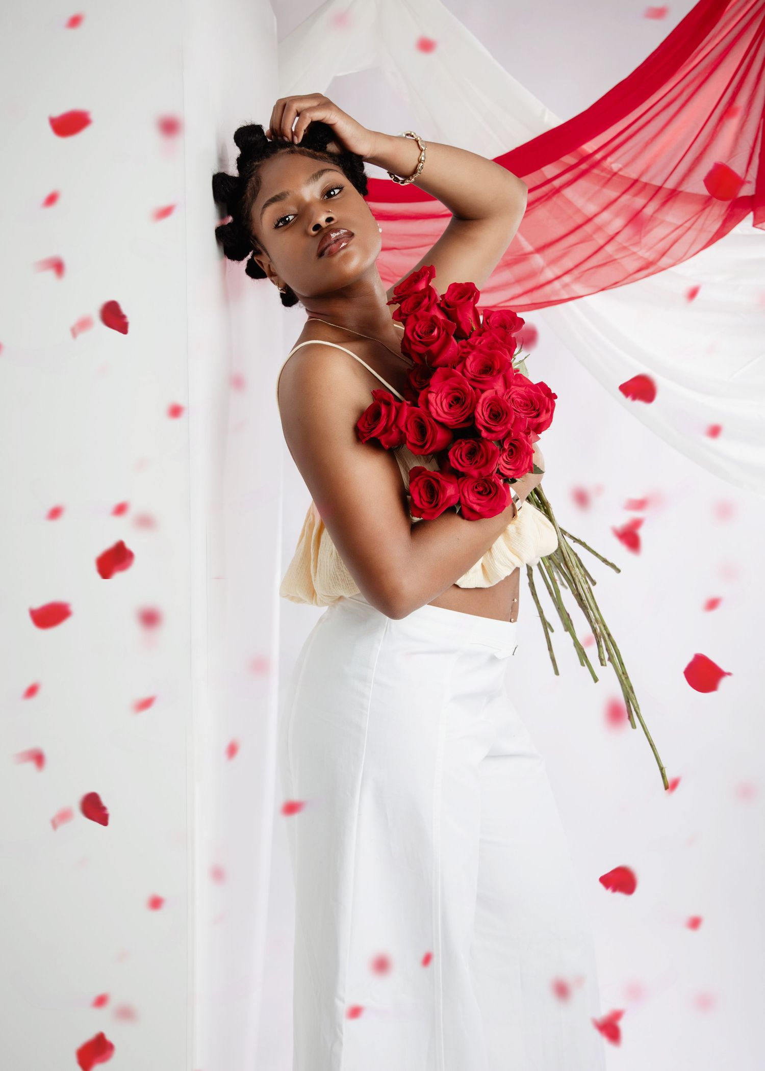 Artistic portrait featuring red roses and flowing red fabric against white background with floating rose petals.