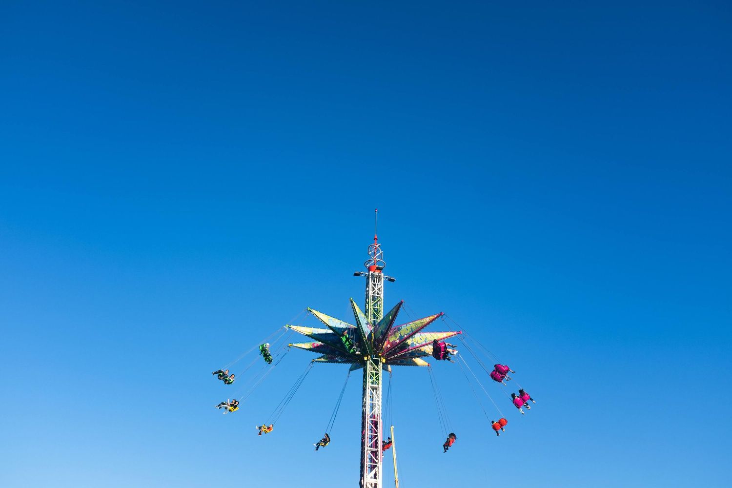 Blue sky view of an amusement park ride with colorful flags spinning photographed by Gia Quilap.