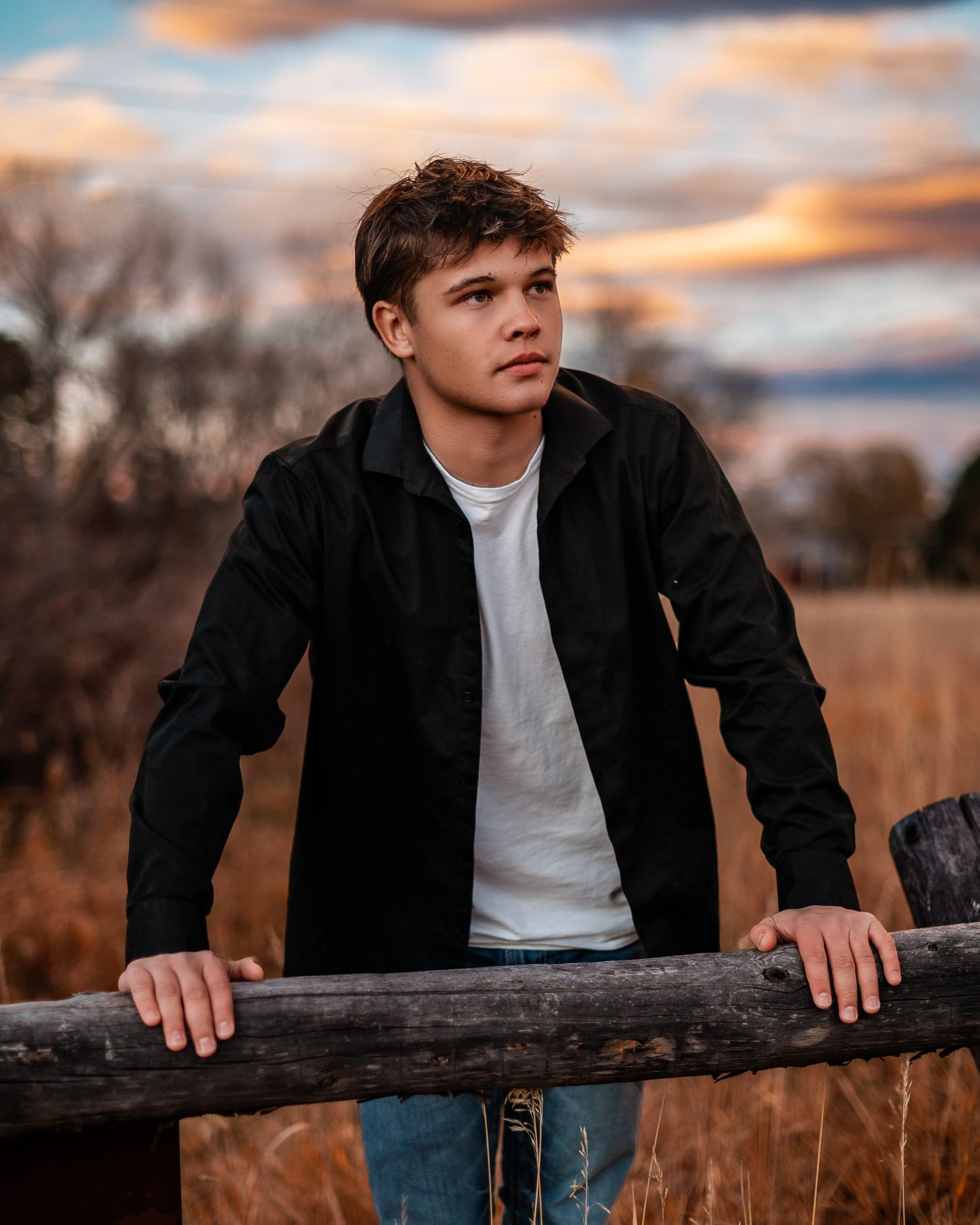 high school senior boy leaning over a fence at sunset