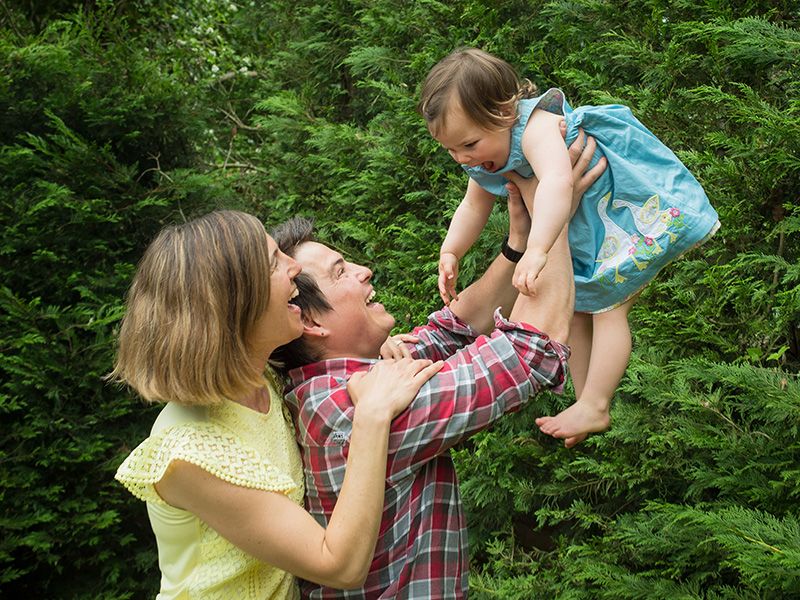 In a garden, a man and woman lift their baby high, capturing a joyful family moment in a portrait by Abigail's studio.