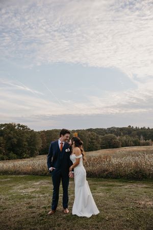 A couple shares a romantic moment in a rustic field with autumn cornfields and trees in the background.