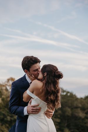A romantic wedding couple shares an intimate kiss during their outdoor celebration at sunset.