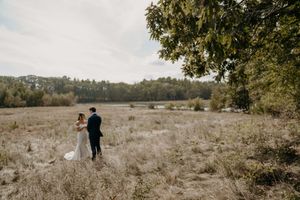 A couple walks together through a serene meadow on an overcast autumn day.