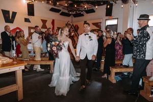 Wedding celebration in a rustic venue with guests cheering as couple walks through during reception.