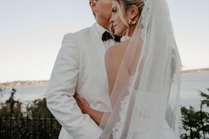 A romantic wedding couple embraces in white attire while standing outdoors during their special day.