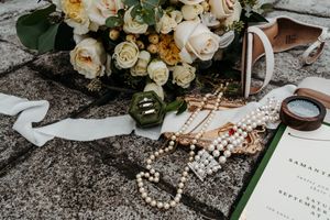 Wedding details including floral arrangements, jewelry, and stationery styled on a rustic stone surface.