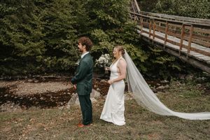A couple shares a tender moment outdoors during their wedding photoshoot in a natural wooded setting.
