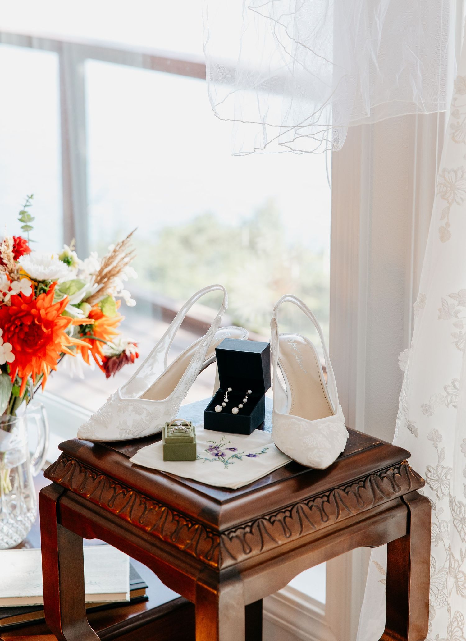 Wedding accessories including white heels and jewelry box arranged on an antique wooden table with floral decor.