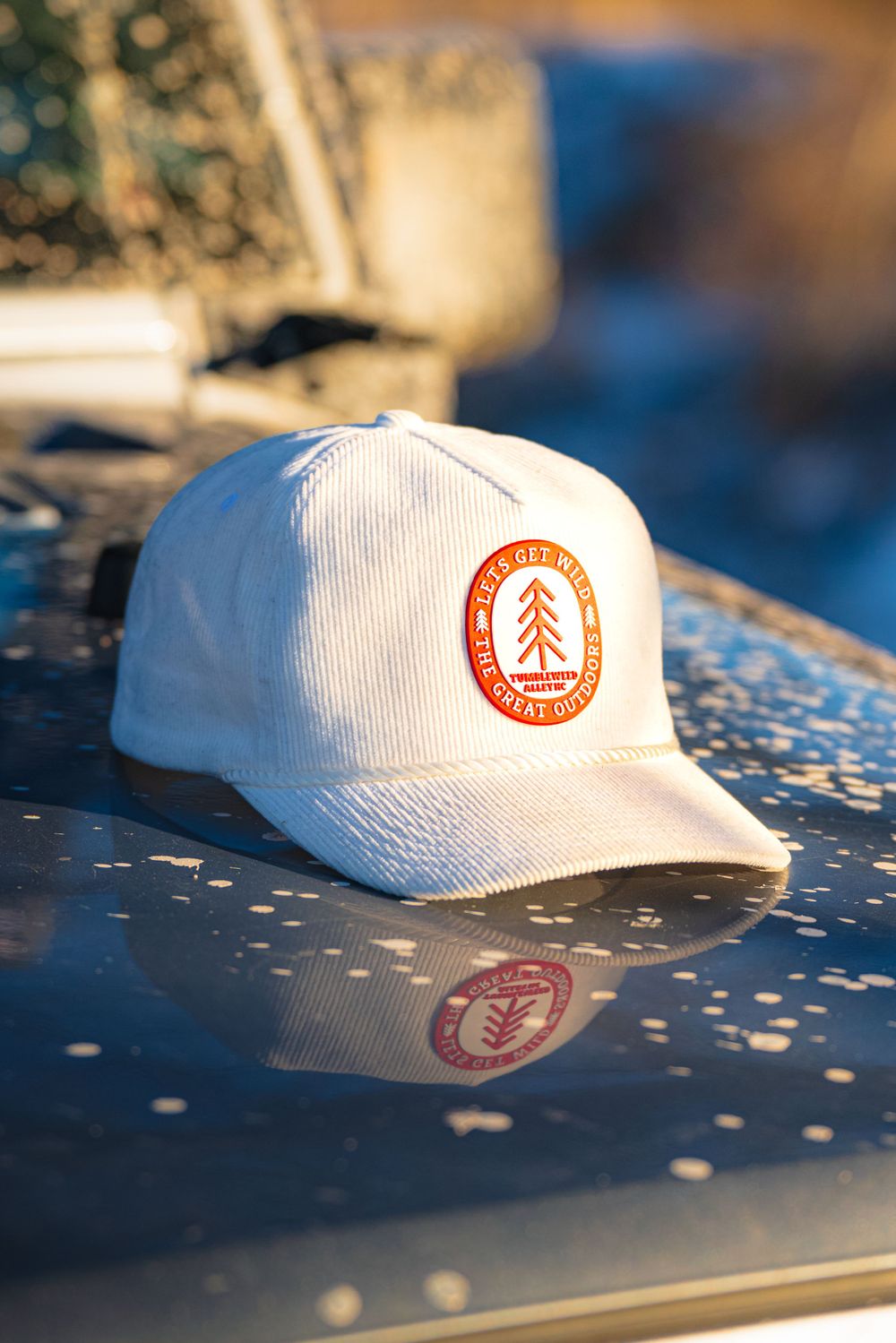 White baseball cap with orange circular forest logo patch sitting on reflective surface in warm lighting.