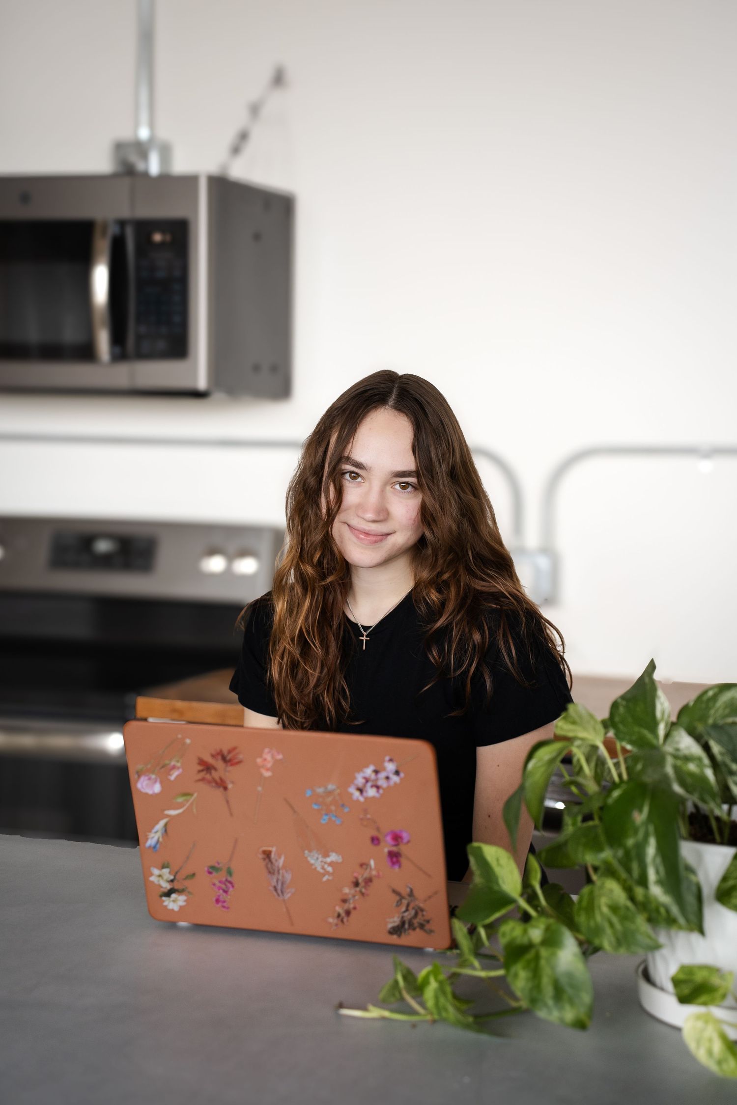 Person working on floral-decorated laptop in modern kitchen with plants.