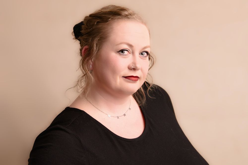 Professional studio portrait of someone wearing a black top against a pale beige background with soft lighting.