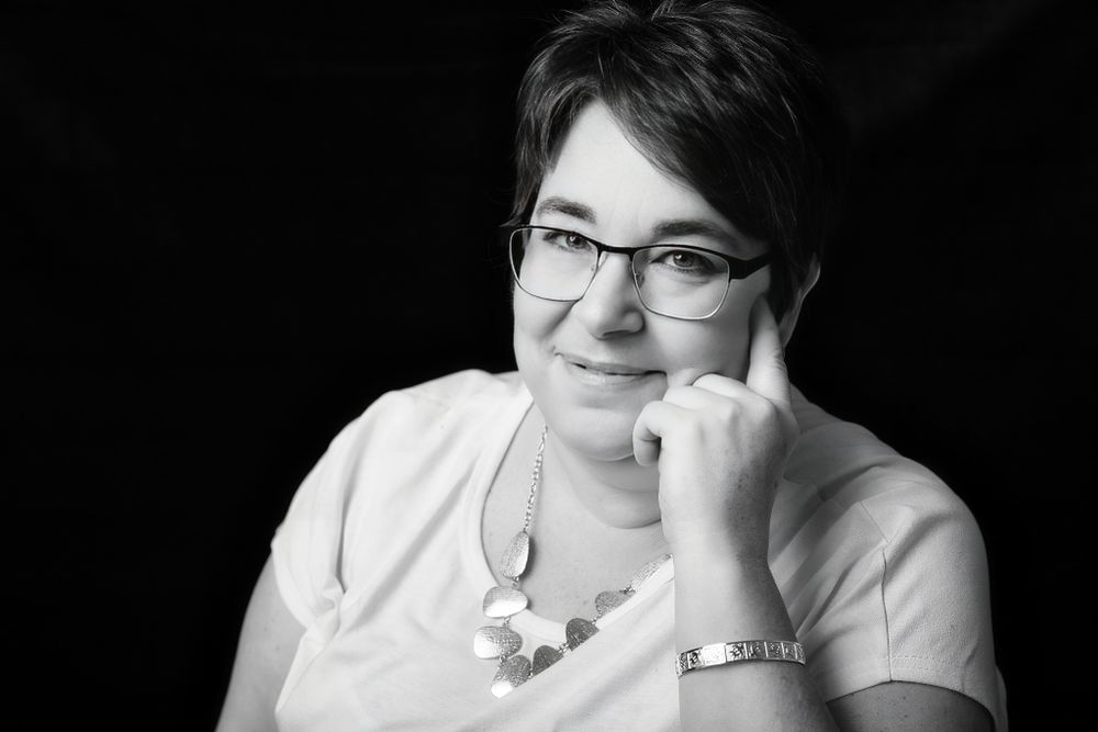 Professional black and white portrait of someone wearing glasses and a white top with a thoughtful expression.