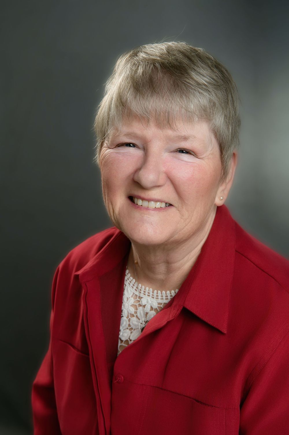 Professional portrait of someone wearing a bright red blazer and floral blouse against a dark background.