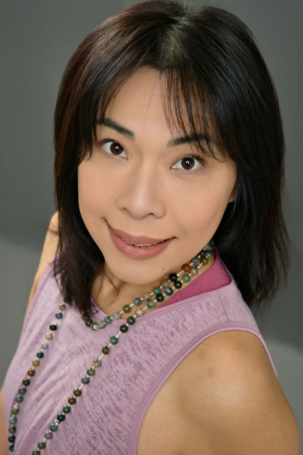 A series of headshots showing someone in a pink top and colorful beaded necklace against a gray background.