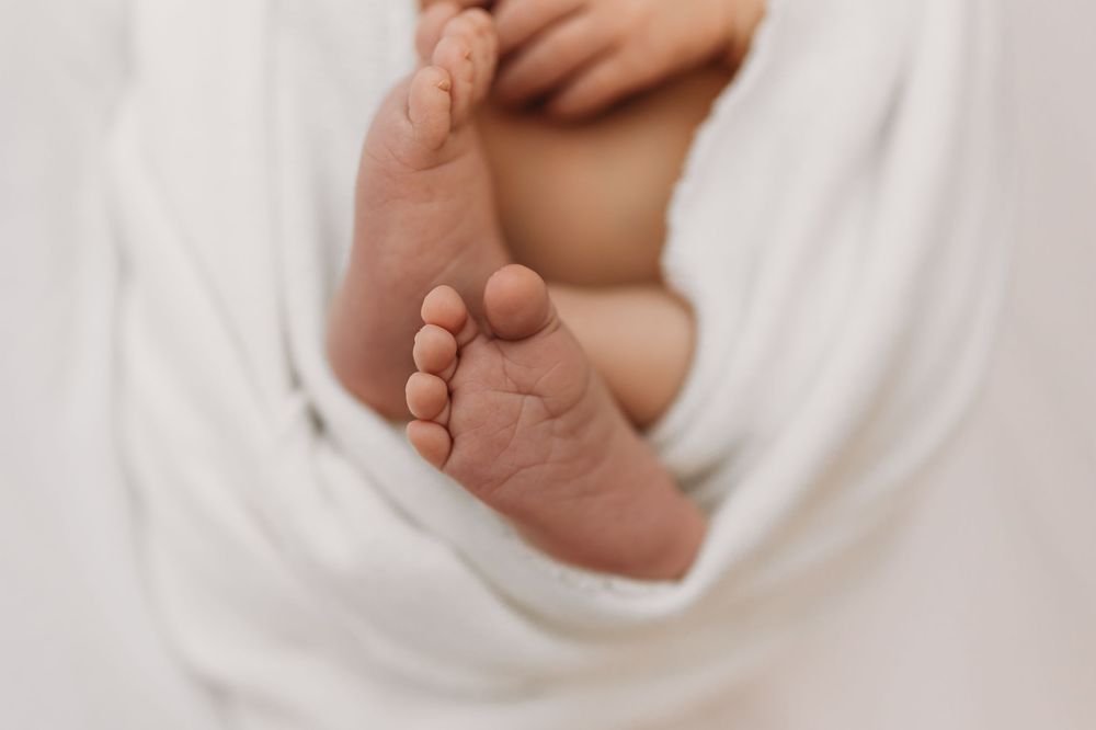 Close-up of newborn baby feet wrapped in a soft white blanket, showcasing tiny toes in a serene setting.