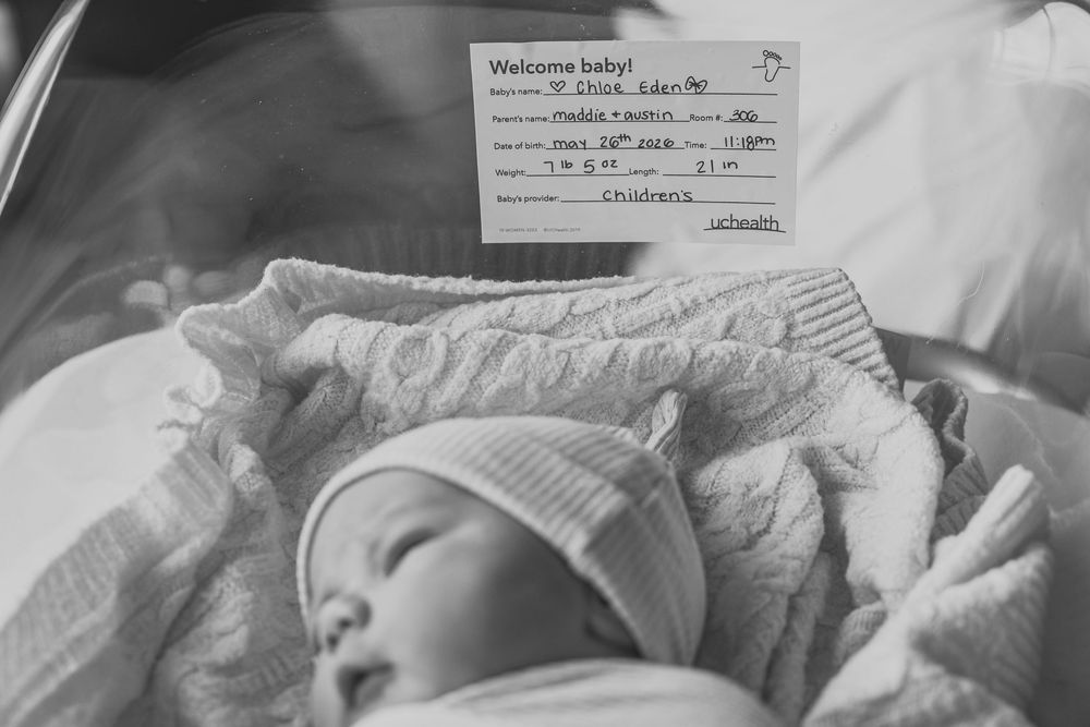 Black and white photo of a sleeping newborn baby in hospital bassinet with welcome baby card.