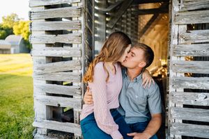 Couple sharing an intimate moment while sitting between rustic wooden slats in a sunlit outdoor setting.