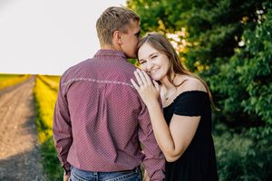 A romantic couple standing on a dirt path share an intimate moment during golden hour.