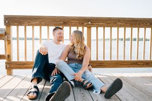 A couple sits casually together on a wooden deck overlooking water.