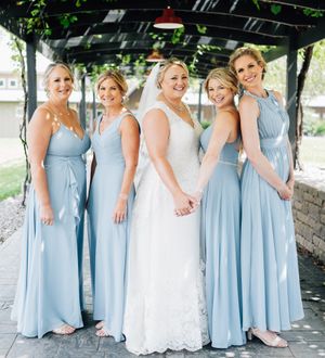 A wedding party poses together wearing light blue floor-length bridesmaid dresses and a white lace wedding gown.